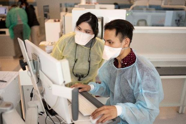 two gowned people at a computer in clinic/lab